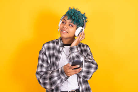 young brunette girl with mobile phone and headphones isolated on color background