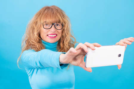 adult or senior woman with smart phone isolated on blue background