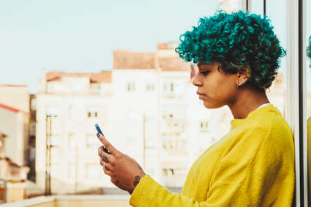 young african american girl with mobile phone outdoors on the terrace of the apartmentの写真素材