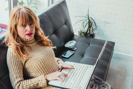 adult woman with laptop at home or apartment sitting on sofa typing