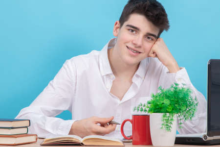 teenage student at the desk with books and laptop on color background
