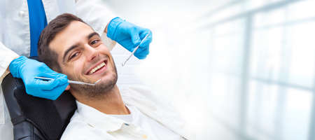 young man in the dental clinic with tools and hands of the dentistの写真素材