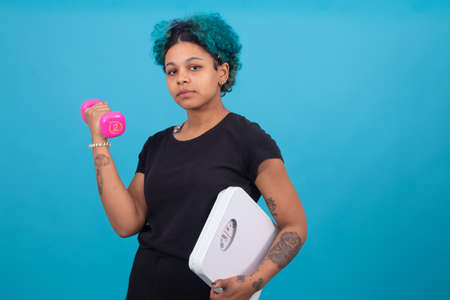 isolated girl with dumbbells and weight scale in color backgroundの写真素材