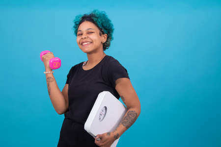 isolated girl with dumbbells and weight scale in color backgroundの写真素材