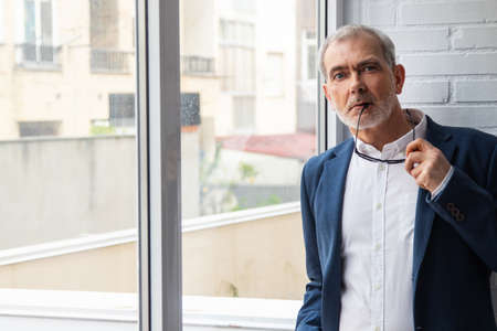 white haired adult or senior man next to window with natural lightの写真素材