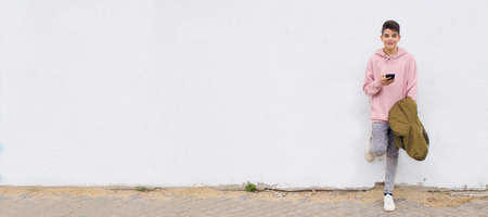 young man with smartphone leaning on street wall