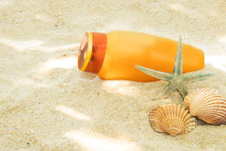 bottle of suntan lotion or sun cream on the beach sand with sea shellの写真素材