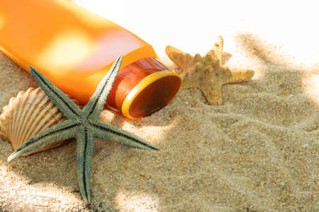 bottle of sunscreen or suntan lotion with star and sea shells on the beach sand