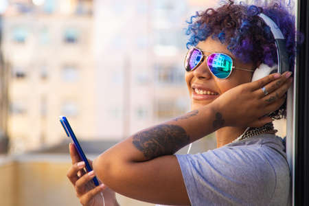 afro american latin girl with mobile phone and headphones on the street outdoors