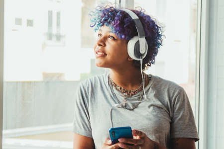 young woman with headphones and mobile phone at the windowの写真素材