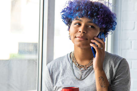 young afro american woman with mobile phone and cup of coffee at the window