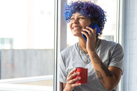 young afro american woman with mobile phone and cup of coffee at the window