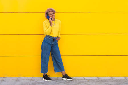 happy girl with mobile phone on yellow city wall