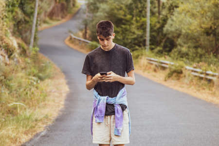 young man outdoors with mobile phone walking on the roadの写真素材
