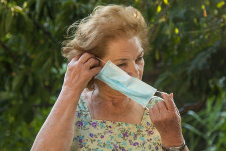 portrait of senior woman putting on face maskの写真素材