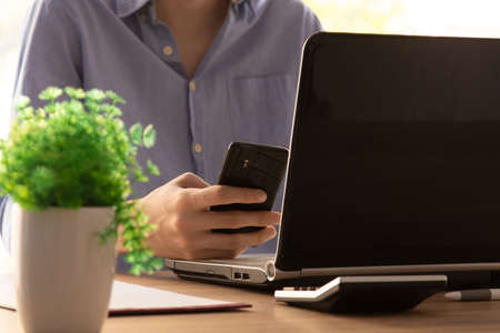 close-up of hand with mobile phone at desk with computer