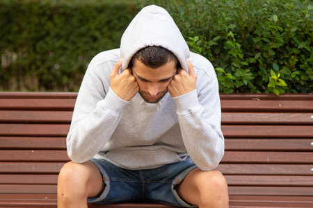 young man sitting on park bench with depressed attitude or loneliness