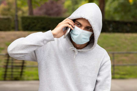 portrait of young man with mask talking on mobile phone in the city outdoors