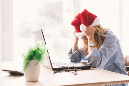 woman with santa claus hat and computer with expression of tired or overwhelmedの写真素材