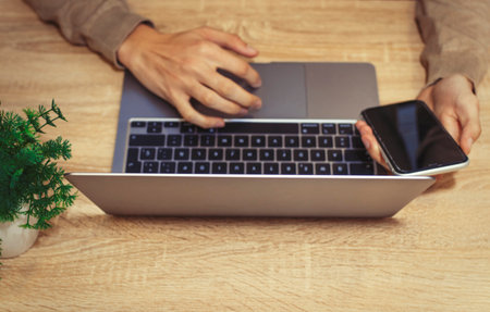 hands on laptop keyboard with mobile phone on desk