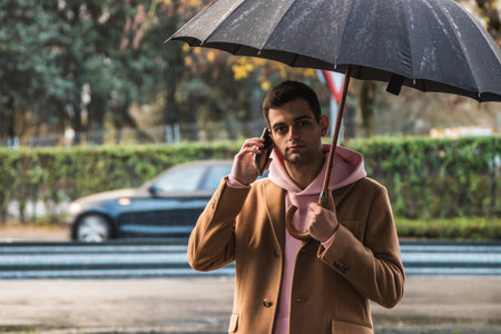 young man on the street raining with umbrella and mobile phone