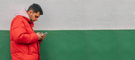 urban casual young man with mobile phone on the wall