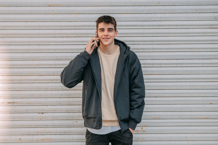 young teenage man talking on mobile phone in front of blind on city street