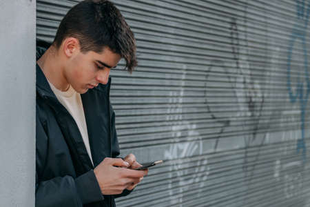 young urban casual style teenager on the street outdoors with mobile phoneの写真素材