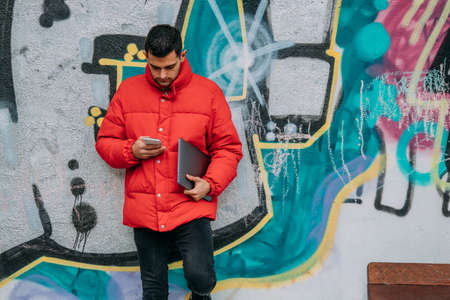 young man with computer and phone on the street wallの写真素材