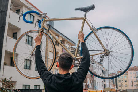 young man lifting the bicycle with his arms in the cityの写真素材