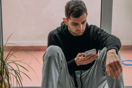 young man at home sitting on the floor with mobile phoneの写真素材