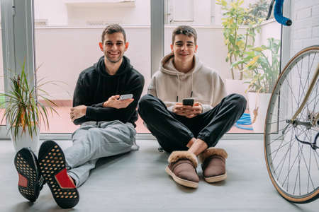 young people at home with mobile phones sitting on the floorの写真素材