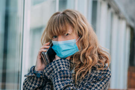 woman with mask and mobile phone in the street outdoorsの写真素材