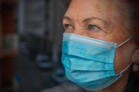 old woman or grandmother with mask at the windowの写真素材