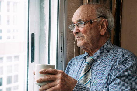 old man with cup of coffee at home windowの写真素材