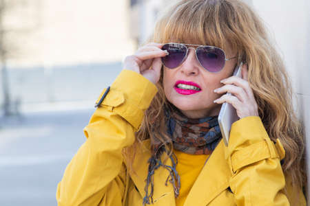 middle aged woman talking on mobile phone in the street wearing sunglassesの写真素材