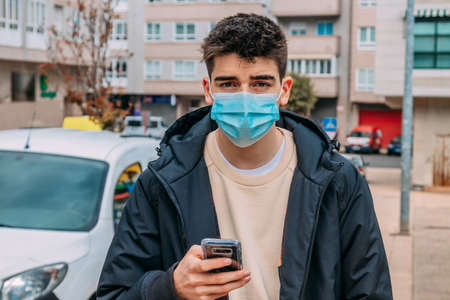 young man with phone and mask walking down the streetの写真素材