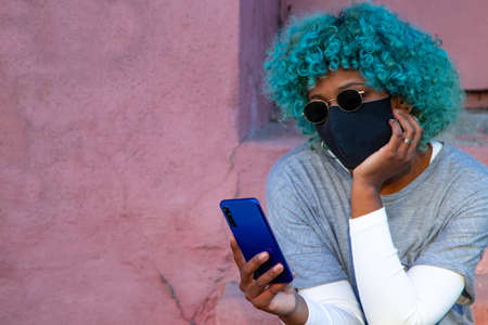 young black african american woman with mobile phone and mask on the street