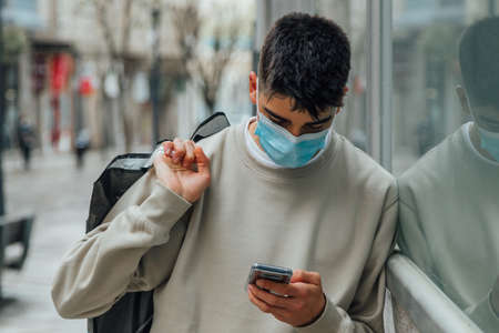 male teenager with mask and mobile phone shopping in the city