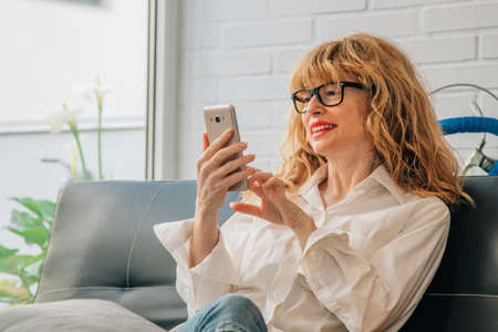 smiling woman with mobile phone on the sofa at home