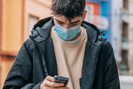 young man with mask and mobile phone on the streetの写真素材