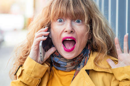 surprised woman talking on mobile phone in the streetの写真素材
