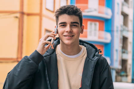 portrait male teenager smiling talking on mobile phone on city streetの写真素材
