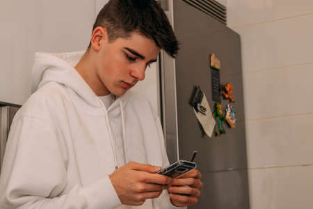 teenage boy with mobile phone in the kitchen at homeの写真素材