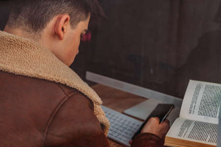 young male at home studying with books and mobile phoneの写真素材