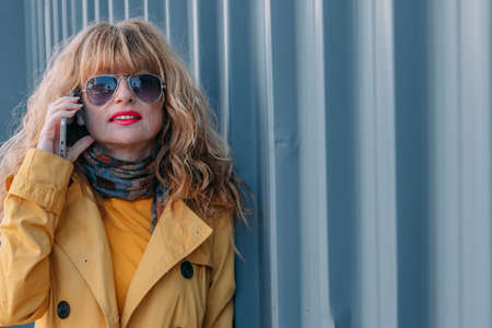 portrait of smiling blonde woman talking on mobile phone in the streetの写真素材