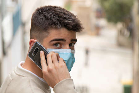 teen boy with mask talking on mobile phone in the city
