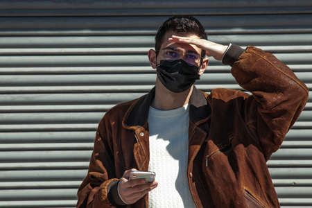 young man with mask and mobile phone on the streetの写真素材