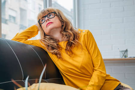 serious adult woman looking out the window sitting on the sofa at homeの写真素材