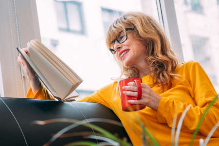 adult woman at home reading a book with cup of coffee or teaの写真素材